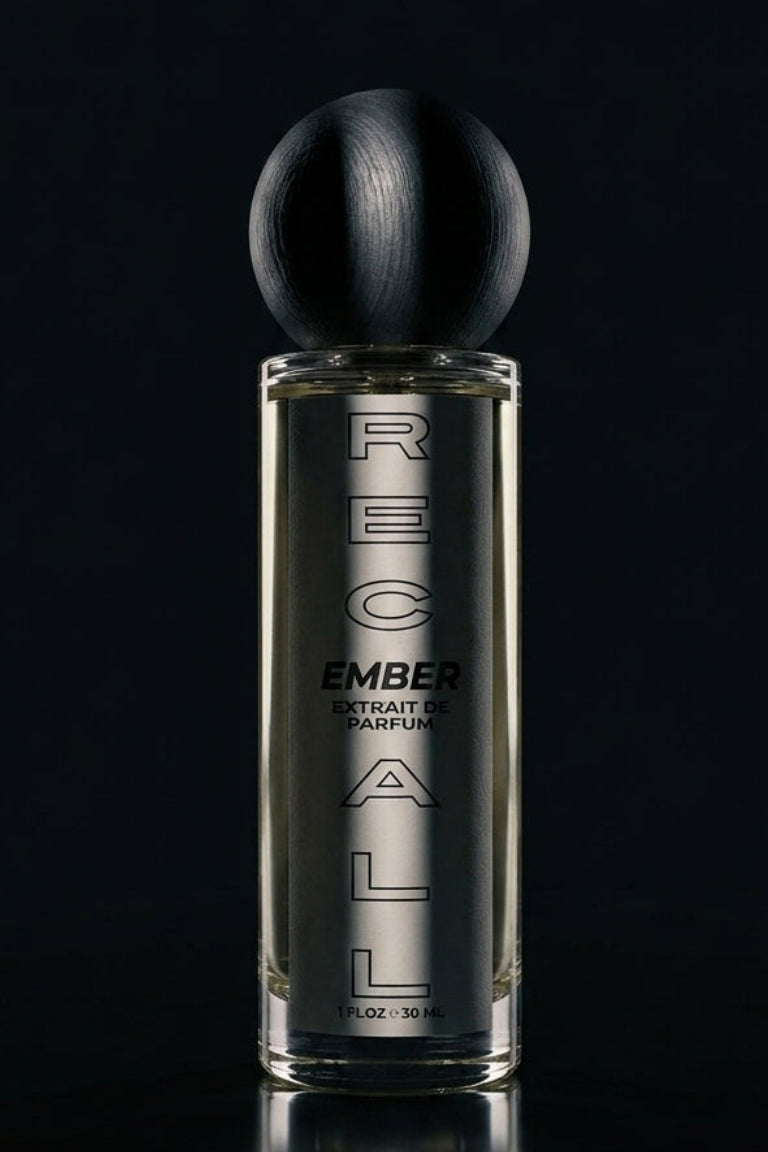 A tall rectangular glass perfume bottle with a spherical black cap, labeled ember extrait de pARFUM, set against a dark black background with a reflective surface below.