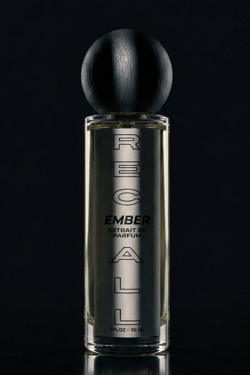 A tall rectangular glass perfume bottle with a spherical black cap, labeled ember extrait de pARFUM, set against a dark black background with a reflective surface below.