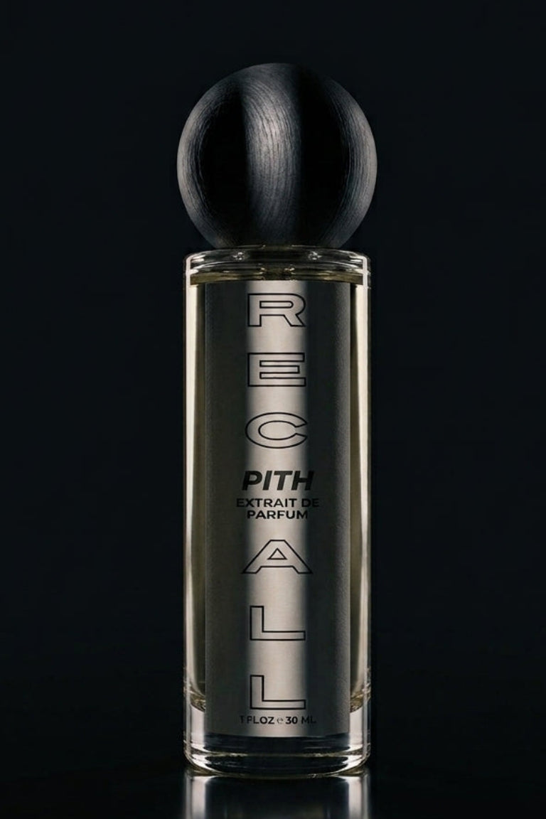 A bottle of RECALL PITH extrait de PARFUM perfume with a black spherical cap and a clear glass body showing the amber liquid inside, set against a dark reflective background.