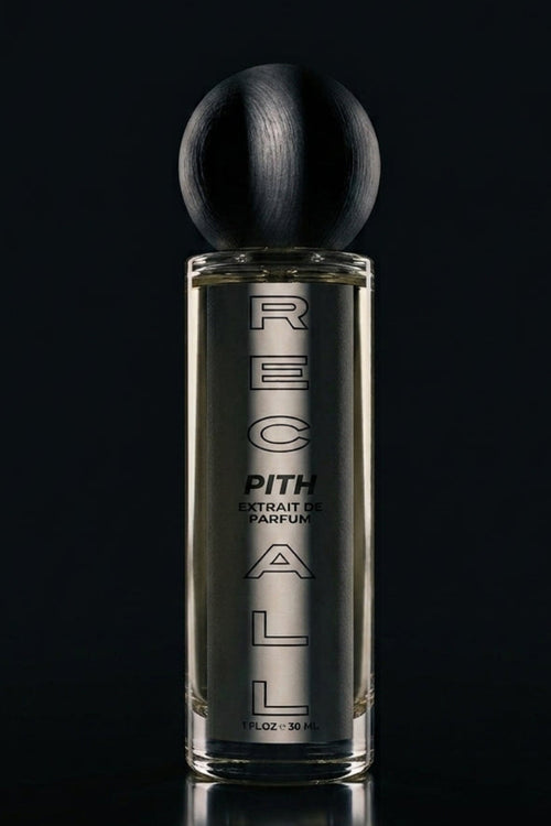 A bottle of RECALL PITH extrait de PARFUM perfume with a black spherical cap and a clear glass body showing the amber liquid inside, set against a dark reflective background.