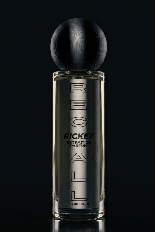 A bottle of Ricky arfum, featuring a clear glass bottle with silver lettering and a black spherical cap, set against a dark reflective background.