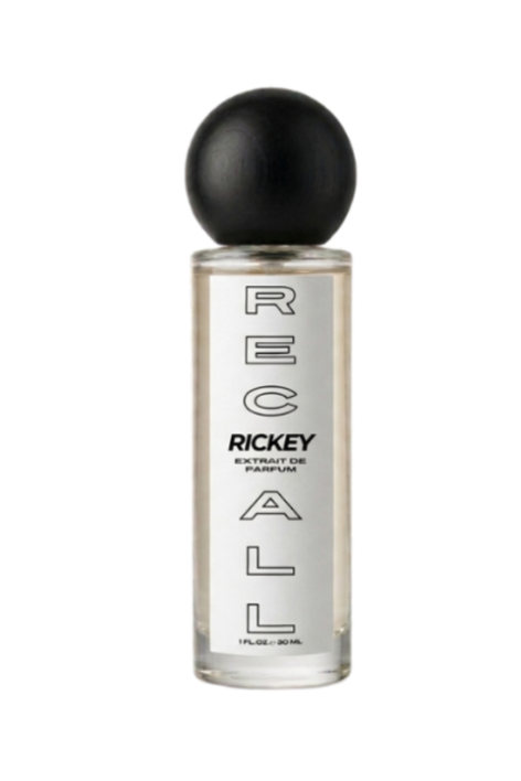 A clear glass bottle of Ricky London 'Recall' perfume with a black spherical cap, shown against a solid white background.